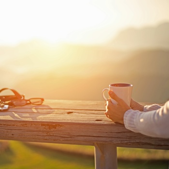 Kvinde med et krus kaffe og kamera, der nyder solnedgangen
