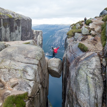 Par på vandretur står på Kjeragbolten med udsigt til Lysefjorden - Norge