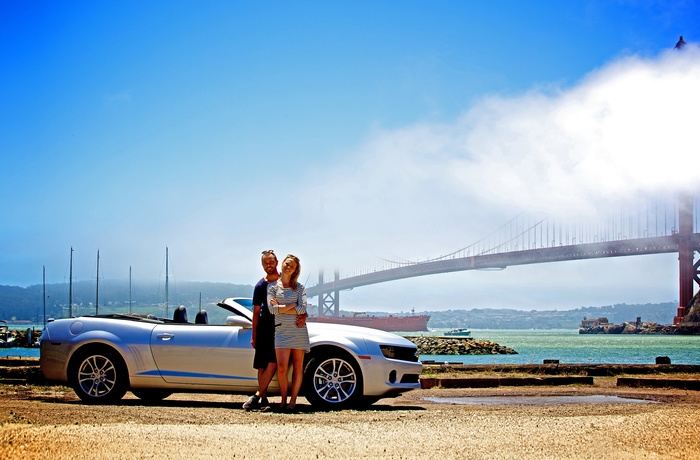 Ungt par foran bil og Golden Gate i San Francisco, USA