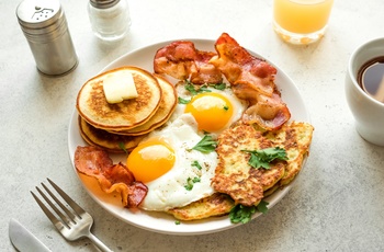 Amerikansk morgenmad med sunny-side æg, hash browns, bacon og pandekager