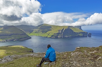 En hiker nyder udsigten til kystbyen Tjørnuvik fra øen Eysturoy, Færøerne