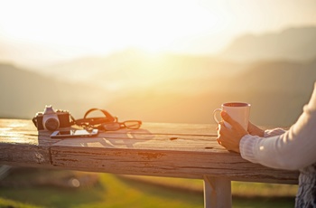 Kvinde med et krus kaffe og kamera, der nyder solnedgangen
