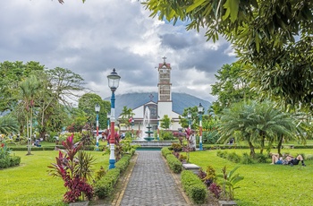 Turister og lokale slapper af på pladsen med kirken i baggrunden i La Fortuna by - Costa Rica