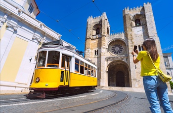 Und kvinde tager billede af Santa Maria katedralen og sporvogn E28 i Lissabon