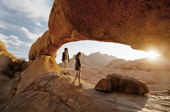 Ungt par vandrer under en af flere naturlige stenbuer i Spitzkoppe, Namibia