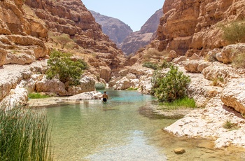 Kvindelig turist tager en dukkert i de naturlige pools i Wadi Shab i Oman