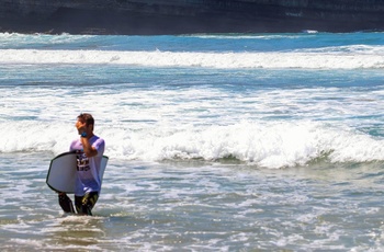 Surfer med fyrtårnet i baggrunden i Biarritz, Frankrig